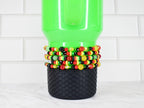 A green tumbler with a black textured base is adorned with several beaded bracelets. The bracelets feature a mix of red, yellow, black, and green beads. The word "IRY" is visible on one of the bracelets.