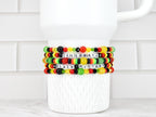 Four beaded bracelets with the words "CELEBRATE BLACK HISTORY" in white letter beads. The bracelets feature red, yellow, green, and black beads. The bracelets are stacked on a white ceramic mug.