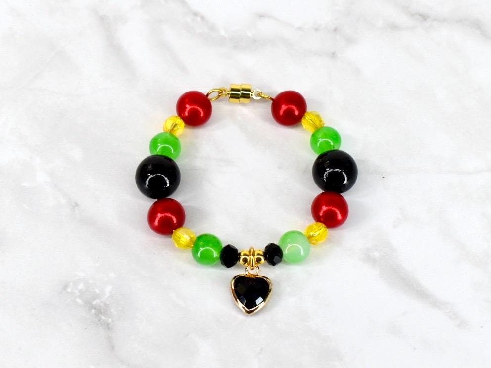 A beaded bracelet featuring red, yellow, green, and black beads. The bracelet has a gold-colored magnetic clasp and a heart-shaped charm with a black center. The beads are round and evenly spaced.