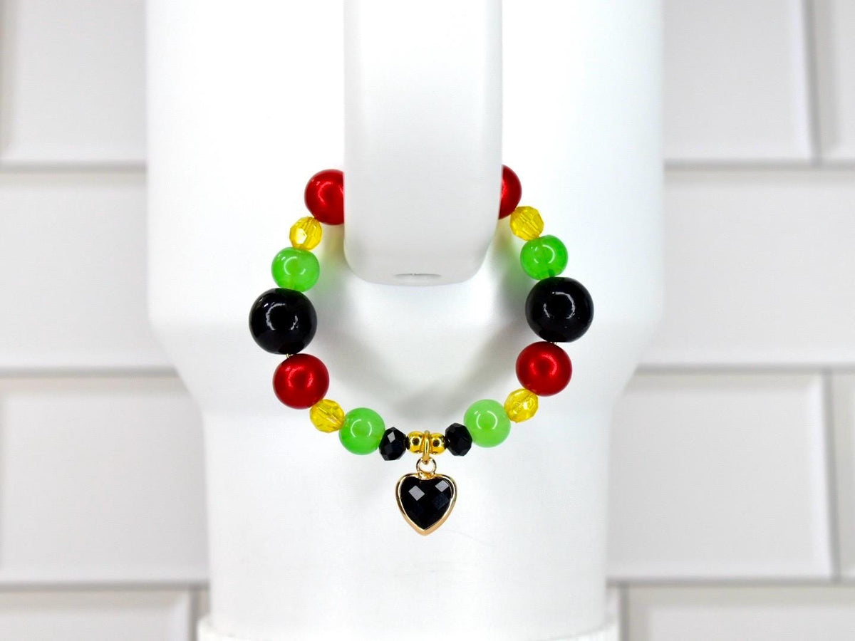 A beaded bracelet featuring red, green, black, and yellow beads. The bracelet has a gold-colored heart charm with a black center. The beads are strung together, creating a colorful accessory.