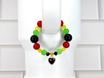 A beaded bracelet featuring red, green, black, and yellow beads. The bracelet has a gold-colored heart charm with a black center. The beads are strung together, creating a colorful accessory.