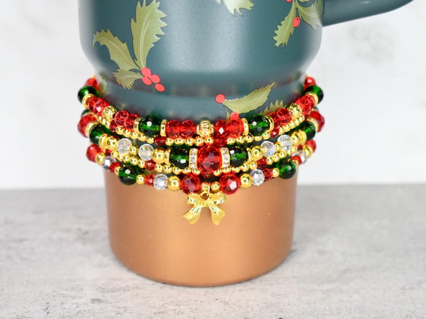 Christmas beaded bracelet stack in holiday colors with gold bow charm, worn as jewelry or wrapped around a tumbler for seasonal accessory styling