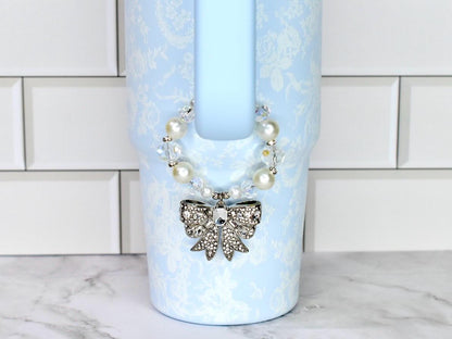 A light blue Stanley with a floral pattern and a decorative bow. The bow is silver with clear rhinestones. The tumbler has a pearl and crystal beaded strap.