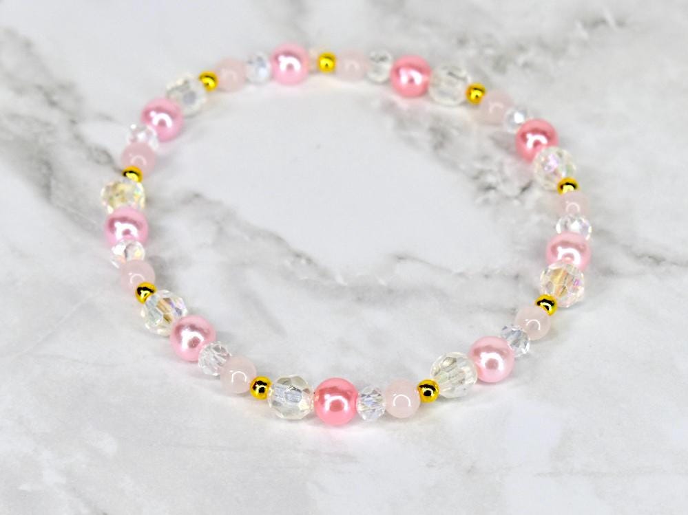 A delicate bracelet featuring a mix of pink, clear, and gold beads. The bracelet includes round pink pearls, clear faceted beads, and small gold-colored spacers. The beads are strung together to form a circular shape.