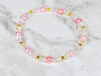 A delicate bracelet featuring a mix of pink, clear, and gold beads. The bracelet includes round pink pearls, clear faceted beads, and small gold-colored spacers. The beads are strung together to form a circular shape.