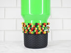 A green tumbler with a black textured base is adorned with several beaded bracelets. The bracelets feature red, yellow, black, and green beads.