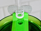 Close-up of a green plastic tumbler lid with a clear plastic straw. The lid has a white ring to hold the straw and a gray fabric patch. The tumbler is green.