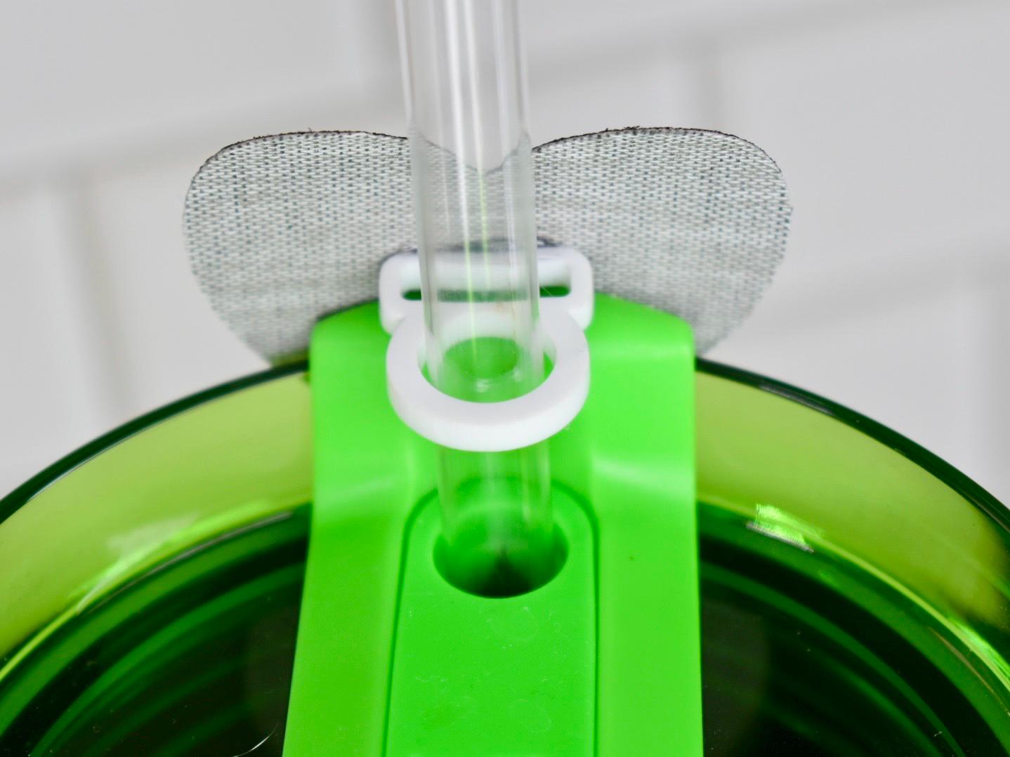 Close-up of a green plastic tumbler lid with a clear plastic straw. The lid has a white ring to hold the straw and a gray fabric patch. The tumbler is green.