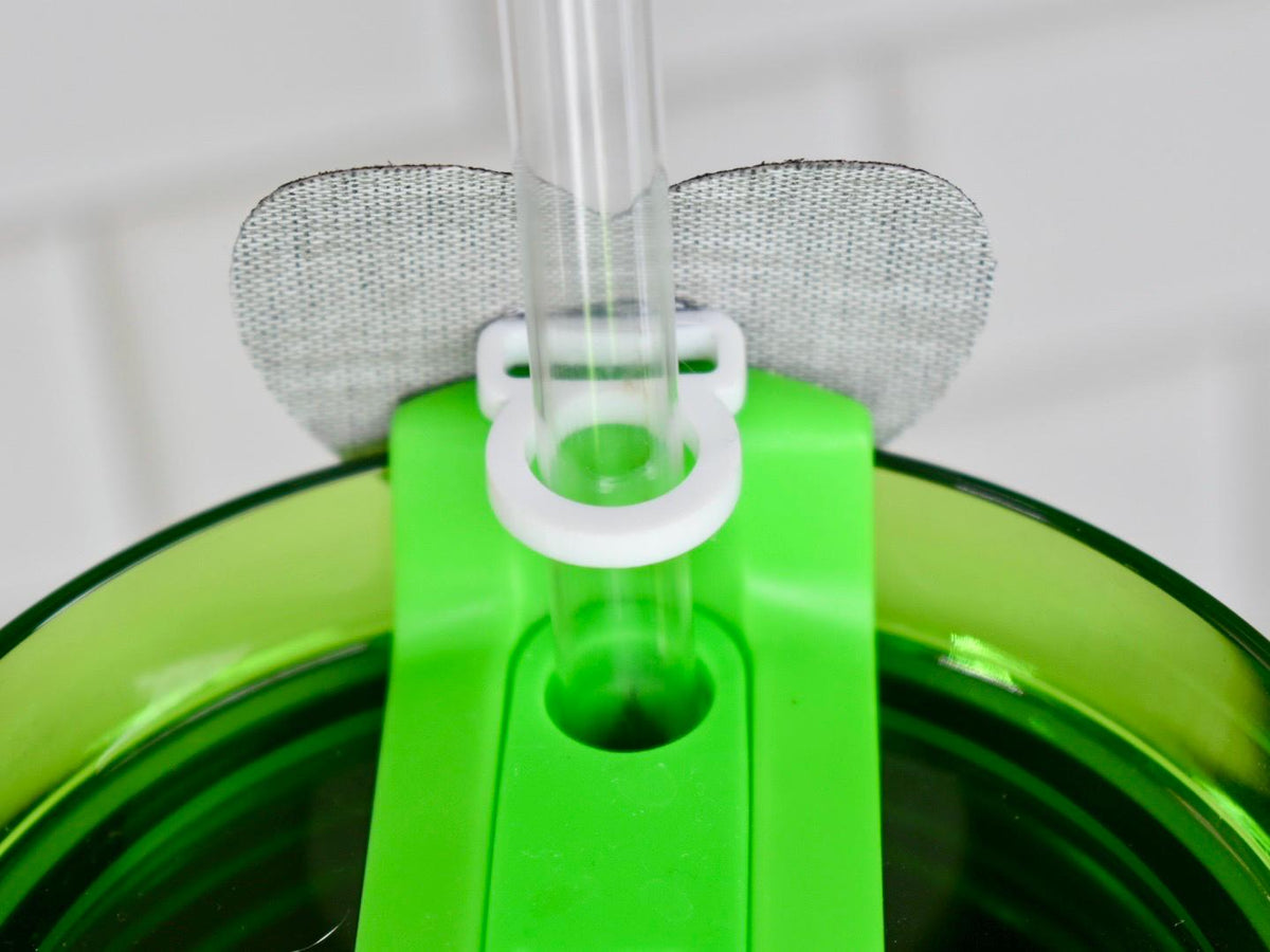 Close-up of a green plastic tumbler lid with a clear plastic straw. The lid has a white ring to hold the straw and a gray fabric patch. The tumbler is green.