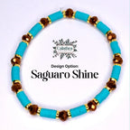 A turquoise beaded bracelet with brown and gold accents. The bracelet features round turquoise beads separated by gold-colored spacers and faceted brown beads. The design is labeled 'Saguaro Shine'.