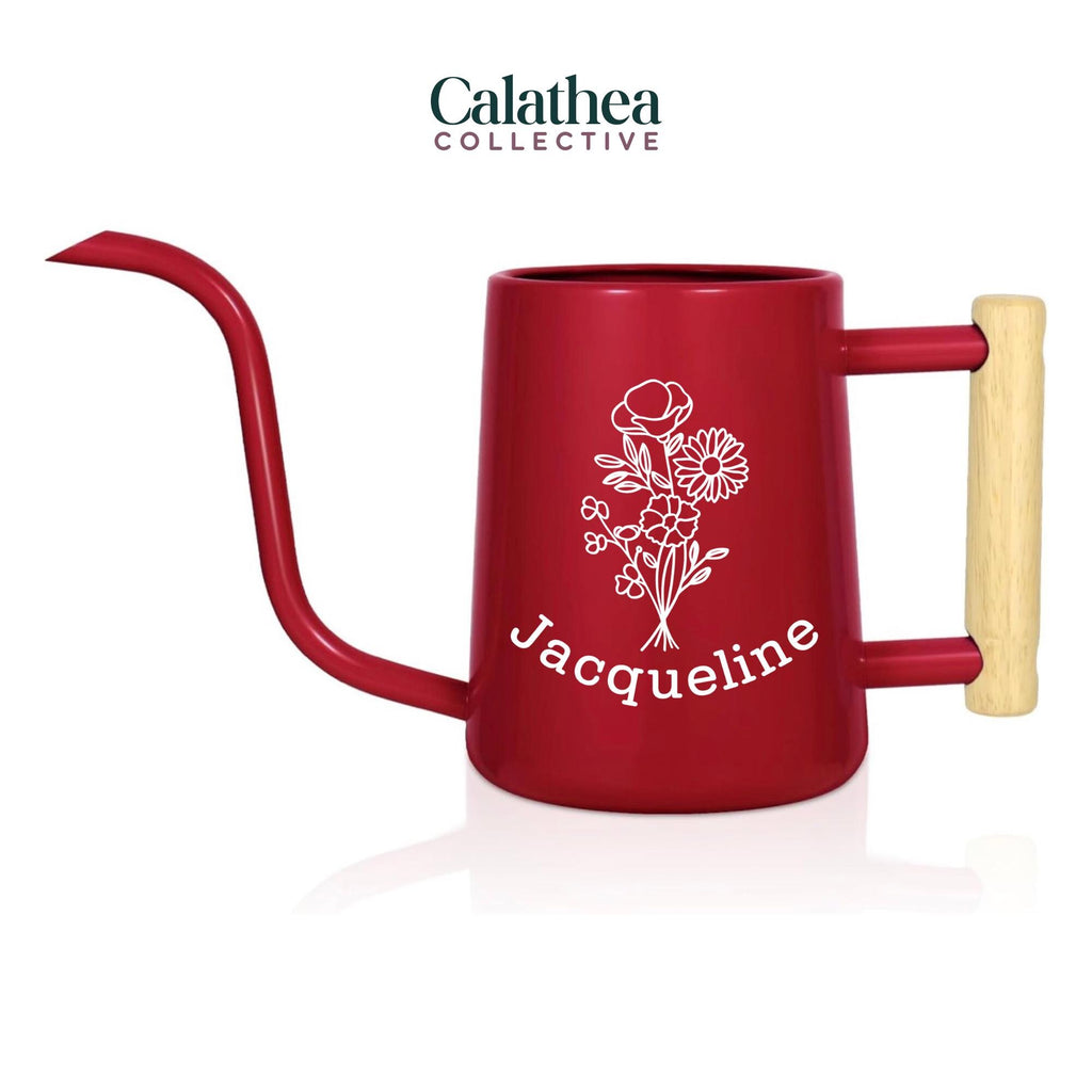 A red metal watering can with long gooseneck spout and wood handle with a white flower bouquet design and 'Jacqueline' below the bouquet in white permanent vinyl.