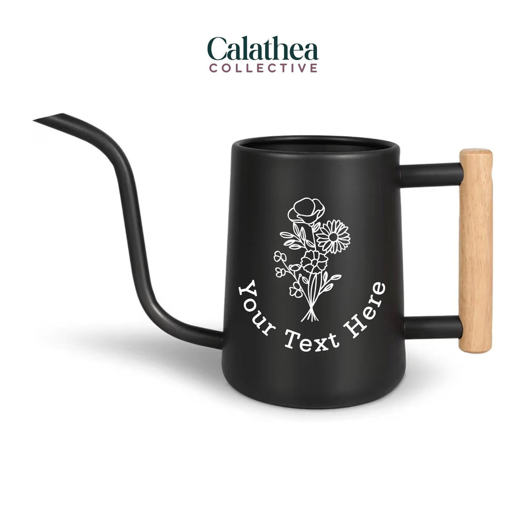 A black watering can with long gooseneck spout and wood handle with a white flower bouquet design and 'your text here' below the bouquet in white permanent vinyl.