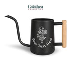 A black watering can with long gooseneck spout and wood handle with a white flower bouquet design and 'your text here' below the bouquet in white permanent vinyl.