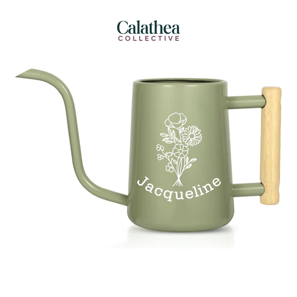 A sage green metal watering can with long gooseneck spout and wood handle with a white flower bouquet design and 'Jacqueline' below the bouquet in white permanent vinyl.