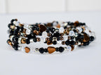 A multi-strand bracelet with black, clear, and bronze beads. The bracelet features heart-shaped charms and metallic accents. The beads are strung together to create a wrap-around design, suitable for wrist sizes of various sizes.