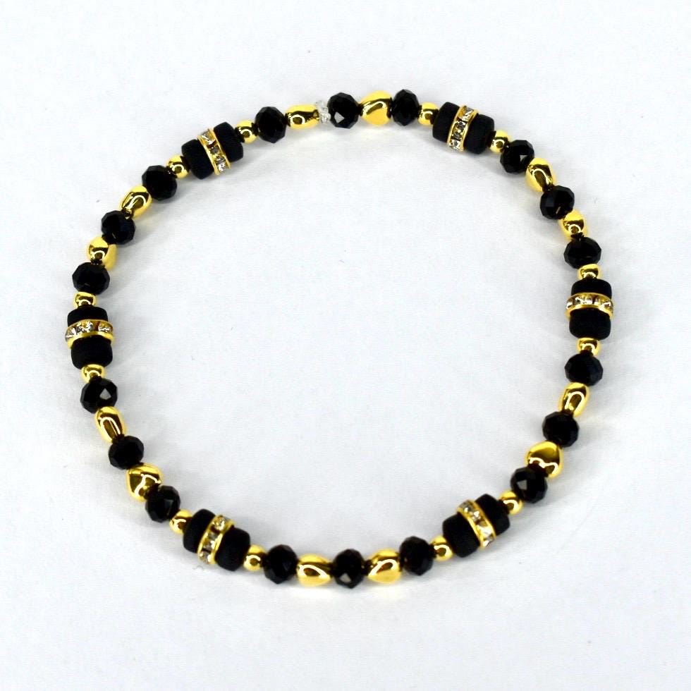 A beaded bracelet featuring black and gold beads. The bracelet has a mix of small, round black beads and larger, rectangular black beads with rhinestone accents. Gold-colored beads separate the black beads.