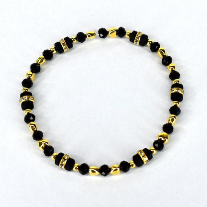 A beaded bracelet featuring black and gold beads. The bracelet has a mix of small, round black beads and larger, rectangular black beads with rhinestone accents. Gold-colored beads separate the black beads.