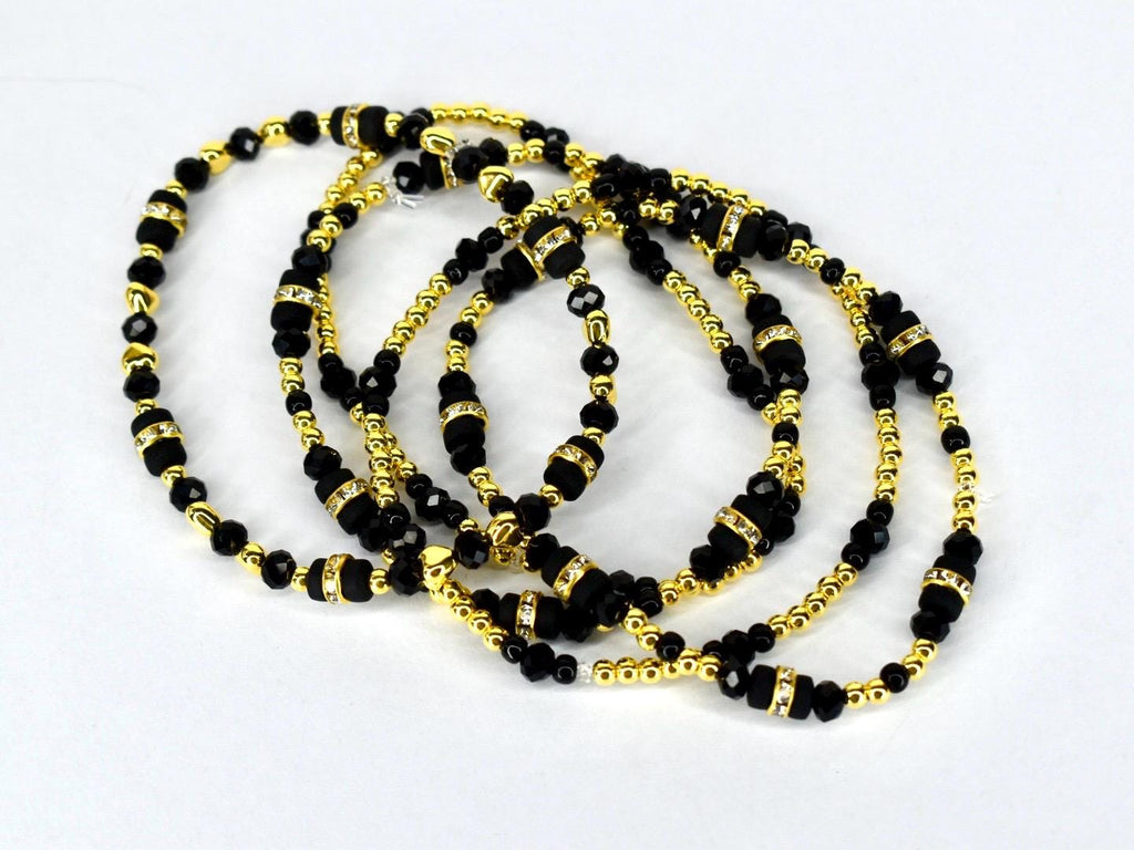 Several strands of black beaded necklaces with gold-colored accents and decorative elements. The necklaces are layered and intertwined, creating a visually rich and elegant display. The beads vary in size and shape.