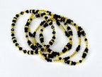 Several strands of black beaded necklaces with gold-colored accents and decorative elements. The necklaces are layered and intertwined, creating a visually rich and elegant display. The beads vary in size and shape.