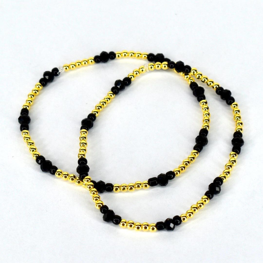 Two beaded bracelets. The bracelets feature a combination of small, gold-colored beads and larger, faceted black beads. The bracelets are displayed on a white background.