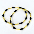 Two beaded bracelets. The bracelets feature a combination of small, gold-colored beads and larger, faceted black beads. The bracelets are displayed on a white background.