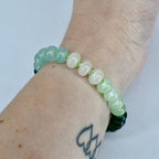 A beaded bracelet featuring a mix of light green and white beads. The bracelet is worn on a wrist, showcasing the varying shades of green and white. The beads are round and smooth, creating a simple yet elegant design.