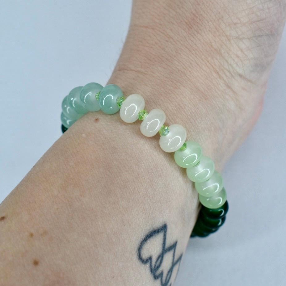 A beaded bracelet featuring a mix of light green and white beads. The bracelet is worn on a wrist, showcasing the varying shades of green and white. The beads are round and smooth, creating a simple yet elegant design.