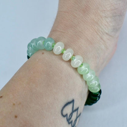 A beaded bracelet featuring a mix of light green and white beads. The bracelet is worn on a wrist, showcasing the varying shades of green and white. The beads are round and smooth, creating a simple yet elegant design.