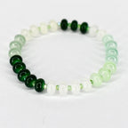 A beaded bracelet featuring a gradient of green and white beads. The bracelet transitions from dark green to light green and white, with a few dark green beads clustered together. The beads are round and strung on a clear elastic cord.