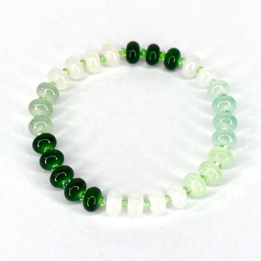 A beaded bracelet featuring a gradient of green and white beads. The bracelet transitions from dark green to light green and white, with small green beads interspersed throughout. The beads are round and smooth, creating a simple yet elegant design.