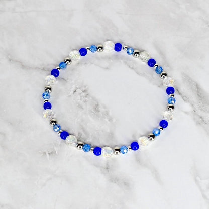 A beaded bracelet featuring a mix of clear, blue, and silver beads. The bracelet is circular and appears to be made of elastic or a similar material. The beads are various sizes and shapes, creating a delicate and elegant look.