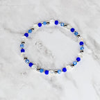 A beaded bracelet featuring a mix of clear, blue, and silver beads. The bracelet is circular and appears to be made of elastic or a similar material. The beads are various sizes and shapes, creating a delicate and elegant look.