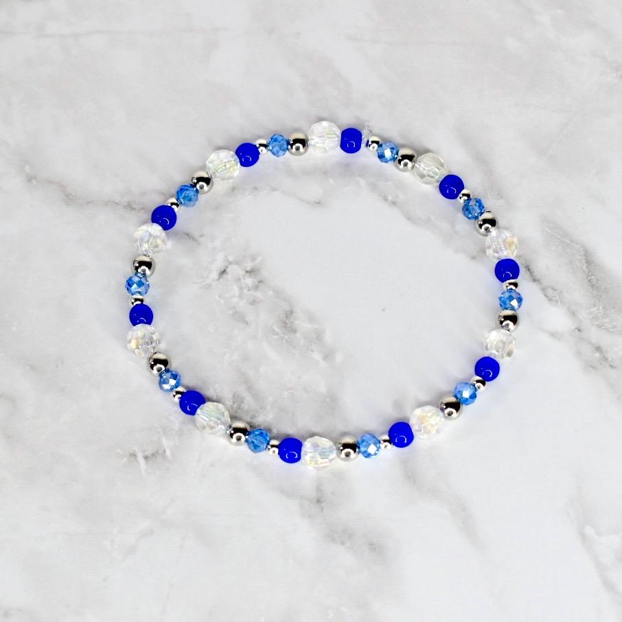 A beaded bracelet featuring a mix of clear, blue, and silver beads. The bracelet is circular and appears to be made of elastic or a similar material. The beads are various sizes and shapes, creating a delicate and elegant look.