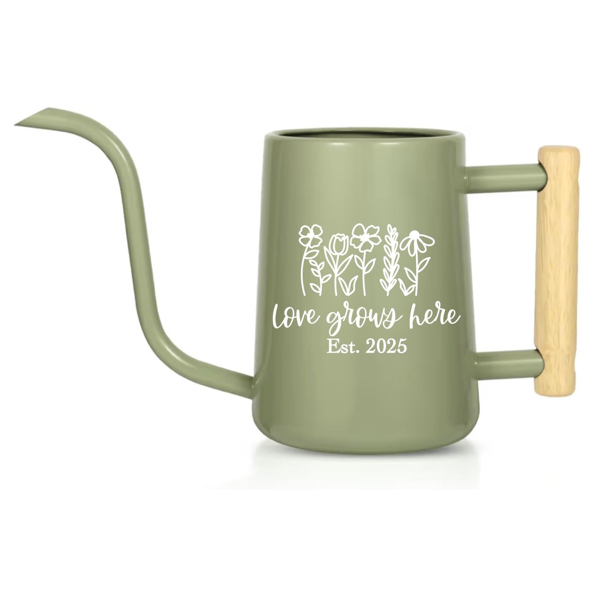Sage green watering can with a long spout and wooden handle. The can features a white floral design and the text "love grows here Est. 2025". A gardening tool for indoor or outdoor use.