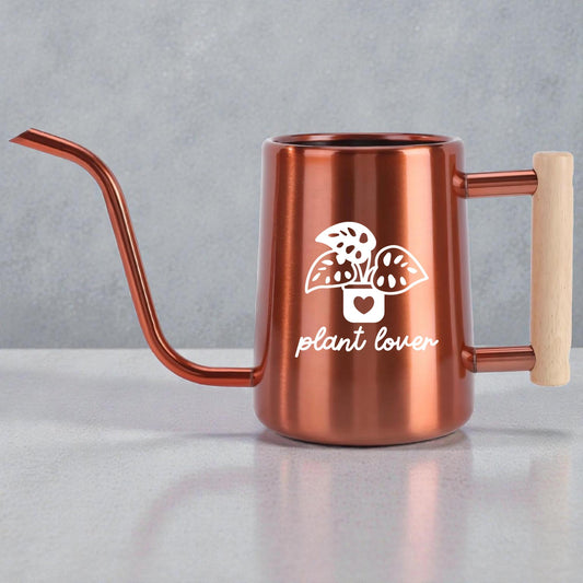 Copper watering can with a long, slender spout and a wooden handle. The can features a white graphic of a potted plant with the words "plant lover" below it. The watering can is designed for indoor or outdoor plant care.