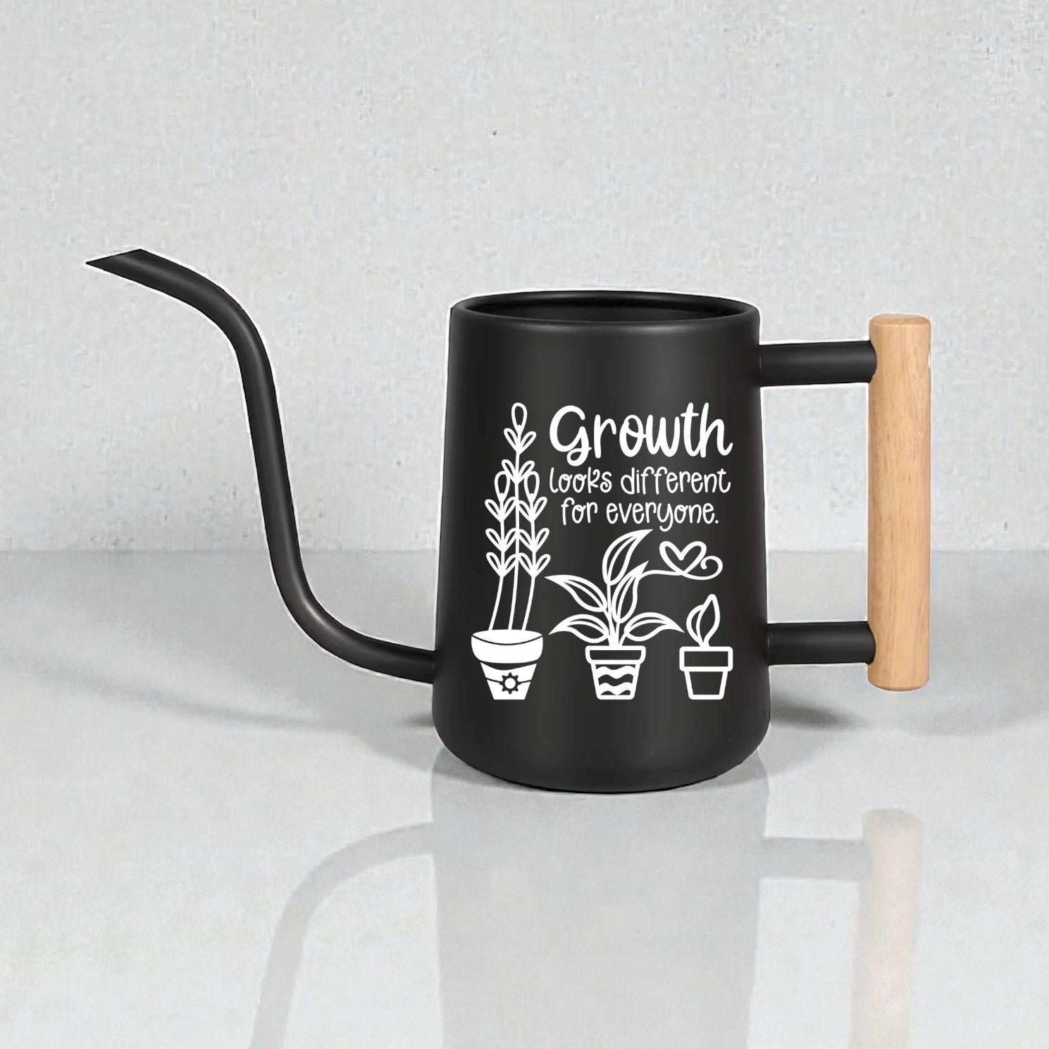Black gooseneck watering can with wood handle. Three house plants are featured as part of the design on the side of the watering can along with the words 'growth looks different for everyone.'