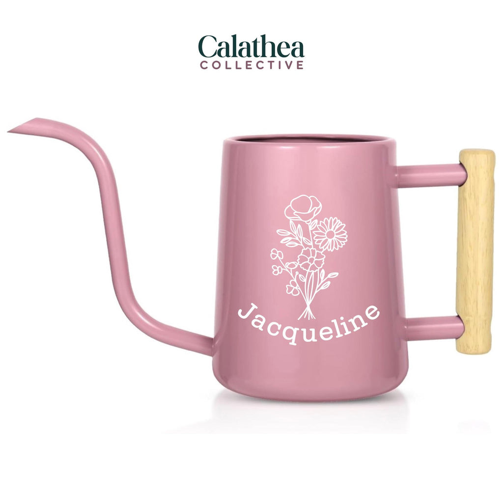 A light pink metal watering can with long gooseneck spout and wood handle with a white flower bouquet design and 'Jacqueline' below the bouquet in white permanent vinyl.
