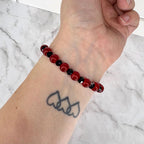 A beaded bracelet featuring a repeating pattern of smooth, round red beads and smaller, faceted black beads. The bracelet is constructed with a flexible cord, allowing it to sit snugly around the wrist, showcasing a high-contrast color scheme.