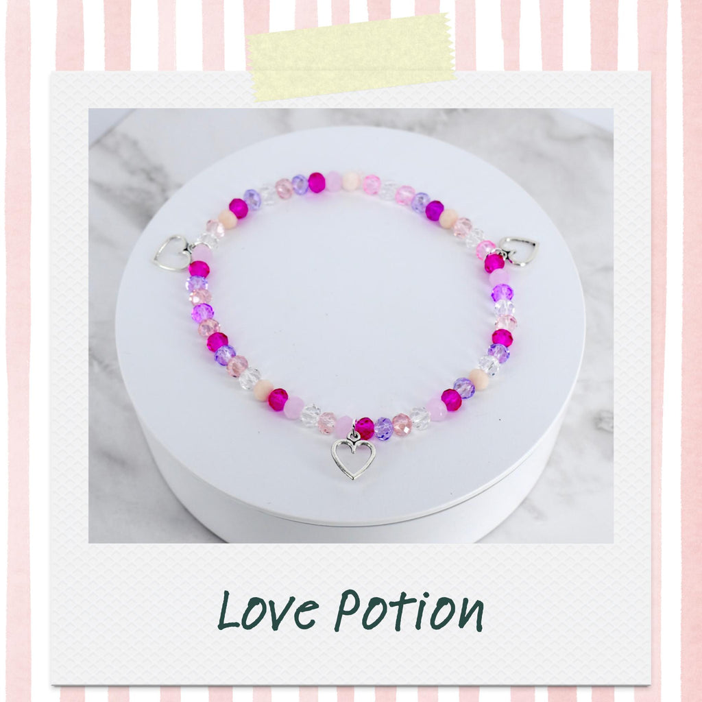 A beaded bracelet with pink, purple, and clear beads. The bracelet has a silver heart charm and heart-shaped clasps. The text "Love Potion" is below the bracelet.