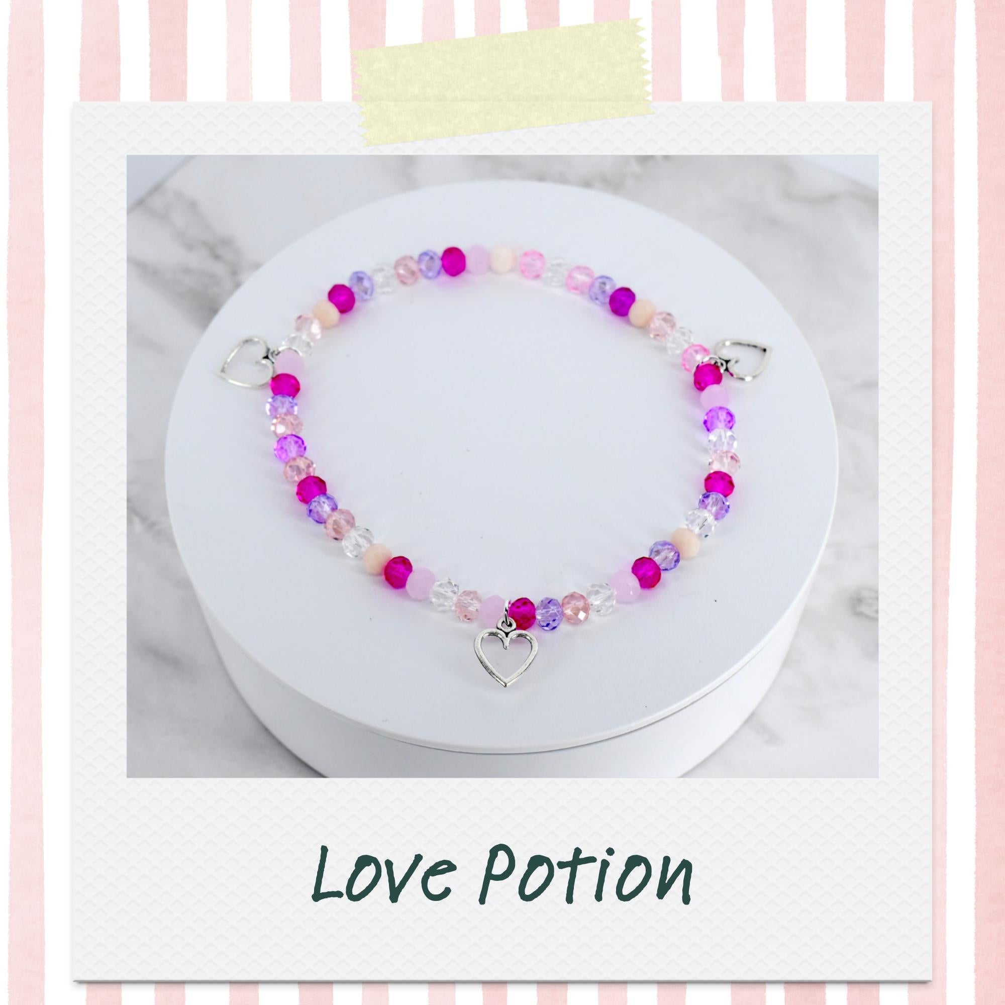 A beaded bracelet with pink, purple, and clear beads. The bracelet has a silver heart charm and heart-shaped clasps. The text "Love Potion" is below the bracelet.