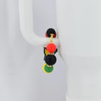 A tumbler bracelet with a gold-colored chain and colorful beads. The bracelet features a black, red, yellow, and green color scheme, with small rhinestones. The bracelet is hanging on a white mug handle.