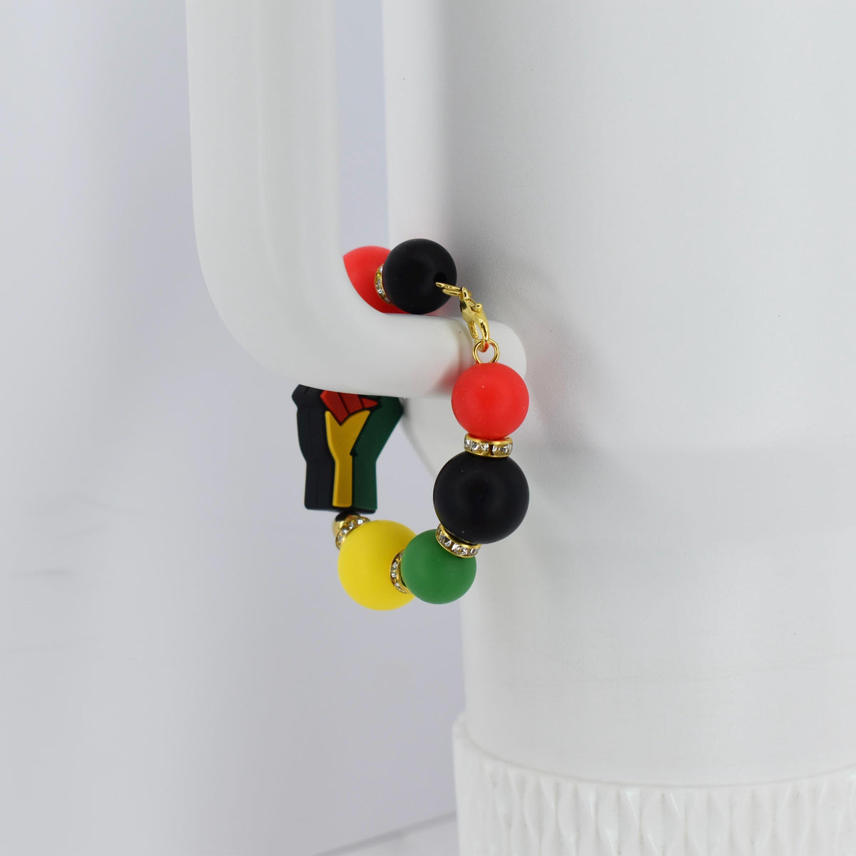 A colorful beaded bracelet featuring red, black, yellow, and green beads. The bracelet includes a charm with a black fist. Gold-colored accents are present throughout the bracelet.