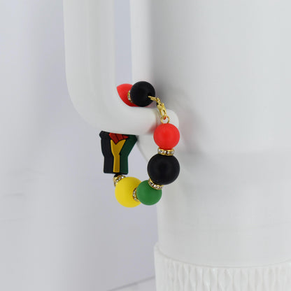 A colorful beaded bracelet featuring red, black, yellow, and green beads. The bracelet includes a charm with a black fist. Gold-colored accents are present throughout the bracelet.