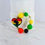 A beaded bracelet featuring a heart-shaped charm with the African continent silhouette in black, yellow, red, and green. The bracelet includes yellow, green, red, and black beads, connected by gold-colored accents and a clasp.