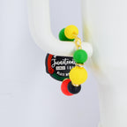 A pair of Juneteenth earrings with a gold chain and colorful beads. The earrings feature green, yellow, red, and black beads. The Juneteenth logo is visible on a black and green tag.
