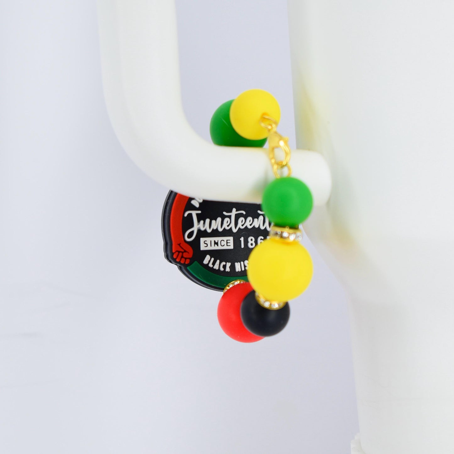 A pair of Juneteenth earrings with a gold chain and colorful beads. The earrings feature green, yellow, red, and black beads. The Juneteenth logo is visible on a black and green tag.