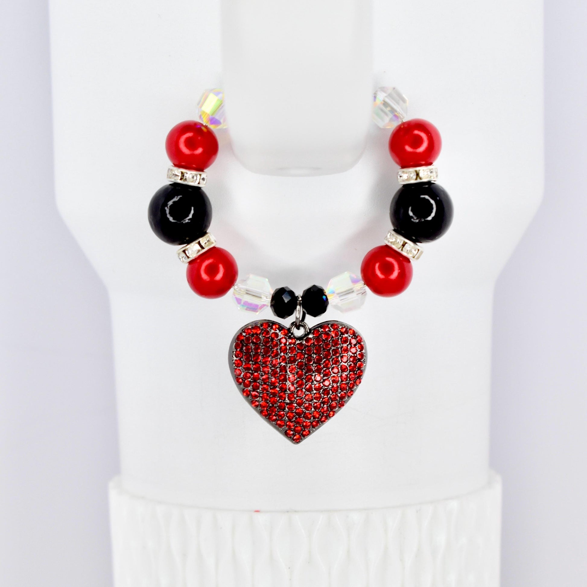 A red heart pendant cup handle bracelet with a beaded design. The bracelet features red and black beads, clear crystal accents, and a heart-shaped pendant covered in red rhinestones. The bracelet is displayed on a white surface.