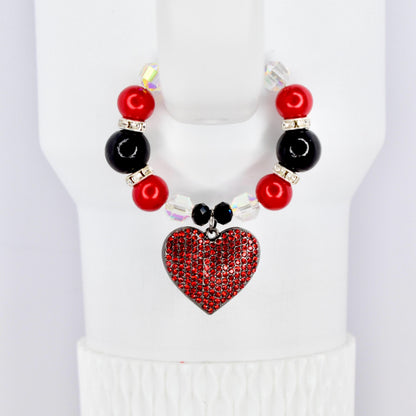 A red heart pendant cup handle bracelet with a beaded design. The bracelet features red and black beads, clear crystal accents, and a heart-shaped pendant covered in red rhinestones. The bracelet is displayed on a white surface.