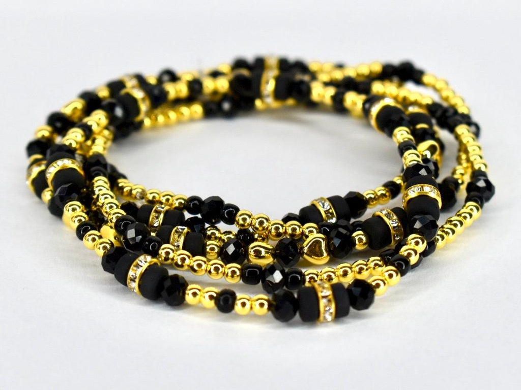 A set of layered waist beads. The beads are a mix of black and gold. Some beads are faceted, and others are round. The gold beads are small and interspersed with larger black beads.