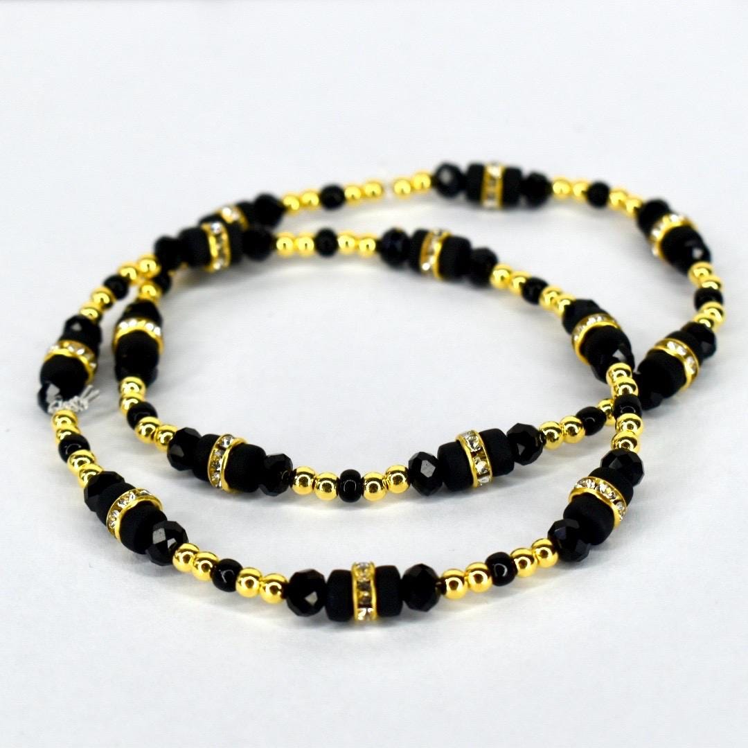 Two beaded bracelets. The bracelets feature black beads interspersed with gold-colored beads and gold-colored spacers with clear rhinestones. The bracelets are displayed on a white background.